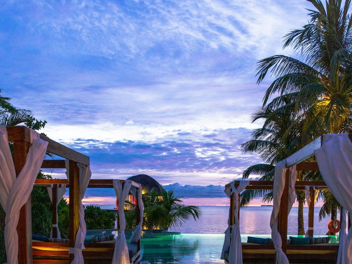 Cliff terrace at dusk — two chairs, two glasses, the horizon