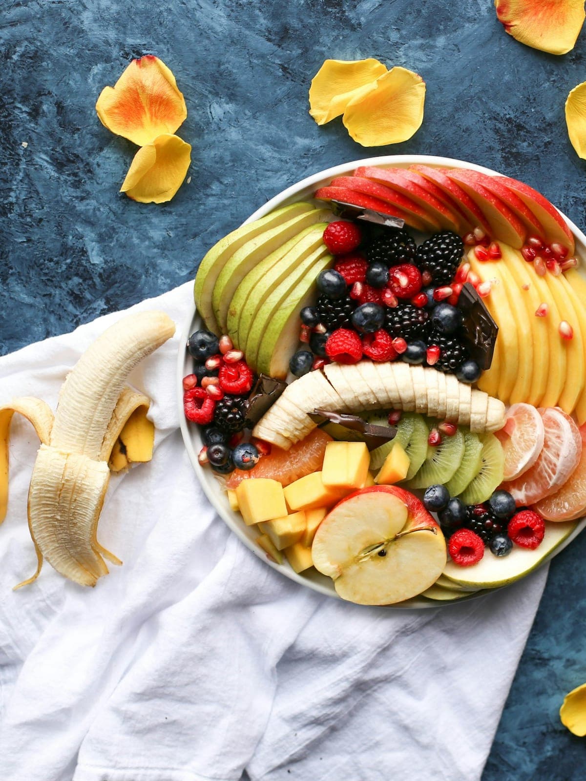 Hands setting a welcome tray — sliced mango, fresh flowers, a handwritten note on cream stationery
